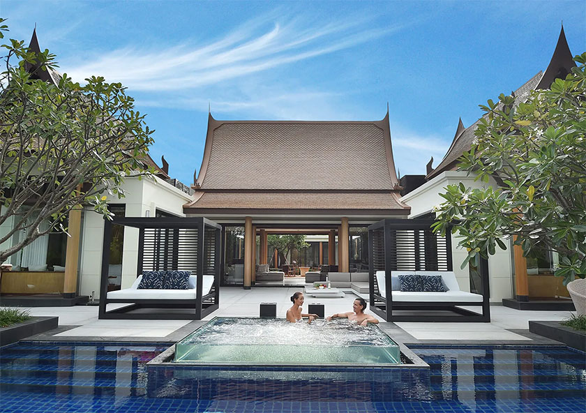 Banyan Tree Grand Residences Grand Villas | Two individuals are conversing in a jacuzzi within a luxurious pool beside a traditional-style building with loungers.