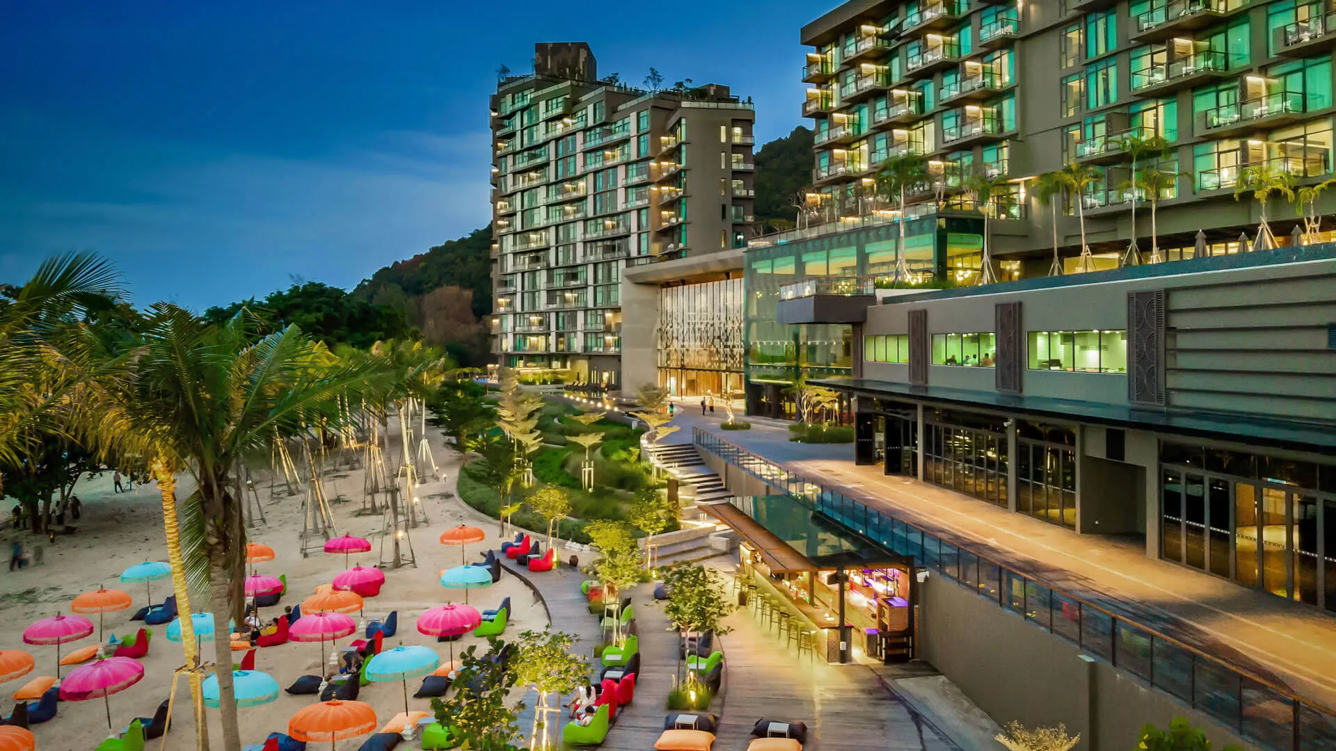 Angsana Residences Teluk Bahang Penang - A modern resort with colorful umbrellas on a beachfront promenade, flanked by a tropical landscape.